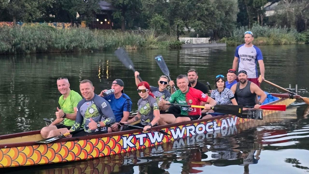 Uśmiechnięta załoga w łodzi z dużym napisem KTW Wrocław na burcie, wieczór na Odrze