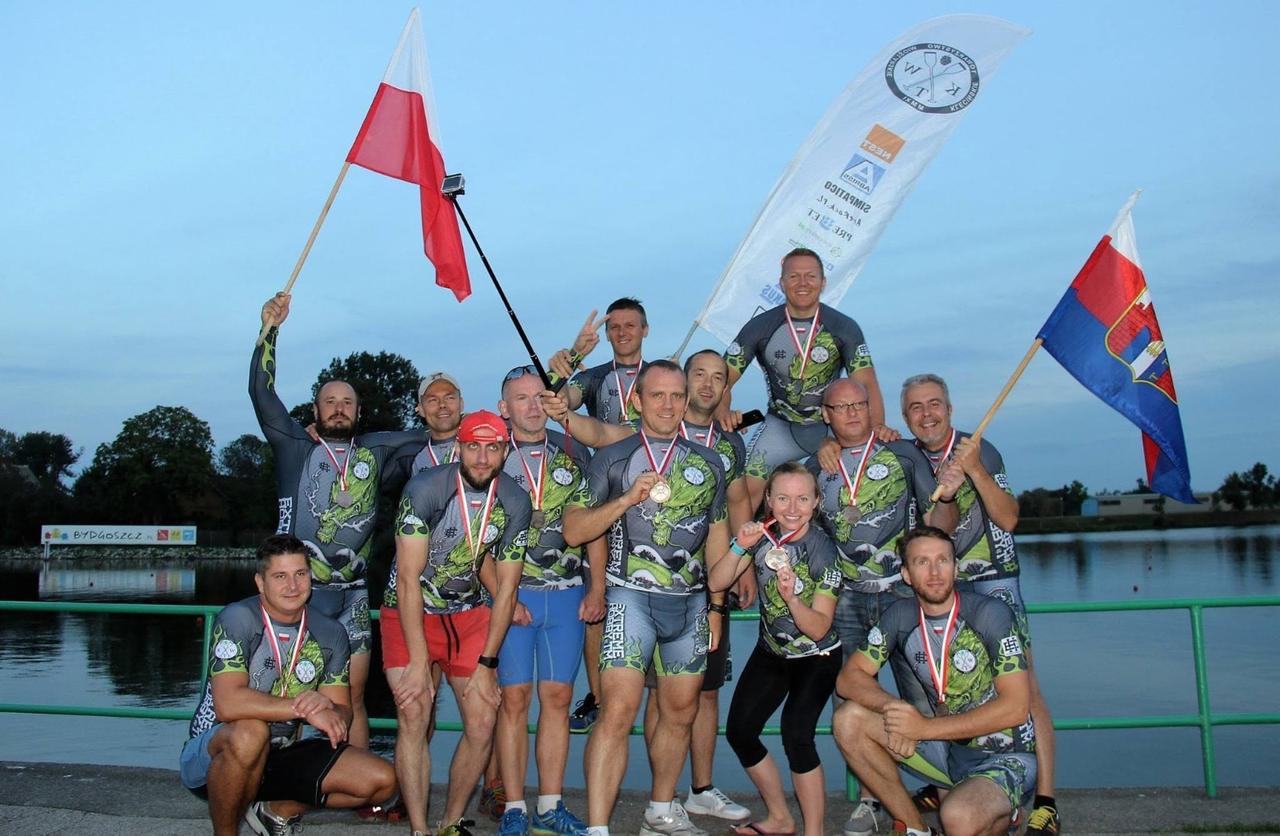 Drużyna KTW z medalami, polską flagą i klubowym banerem nad kanałem o zmierzchu po Mistrzostwach Polski 2016 w Bydgoszczy