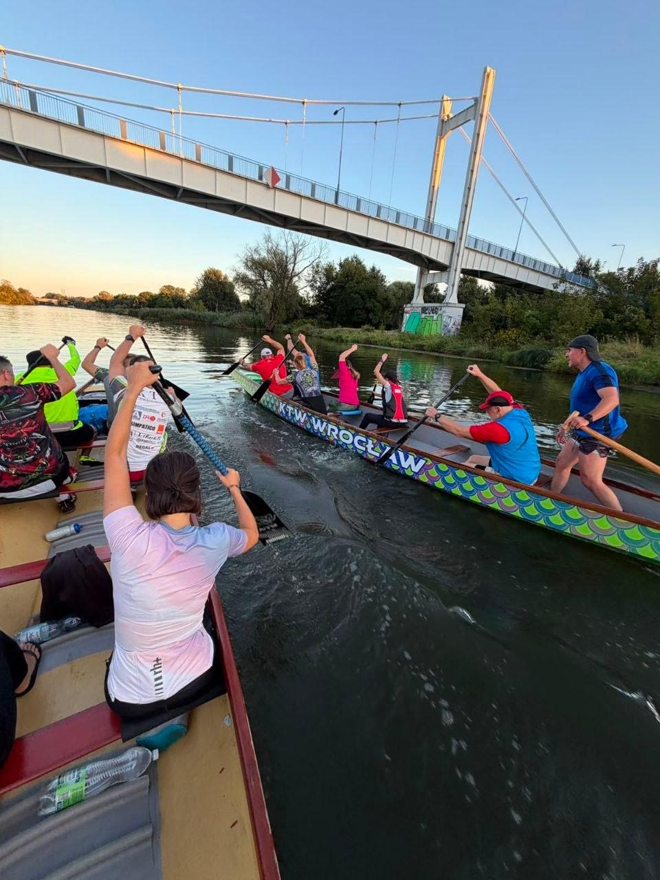 Trening: dwie smocze łodzie KTW płyną obok siebie pod kładką na Odrze, widok z łodzi
